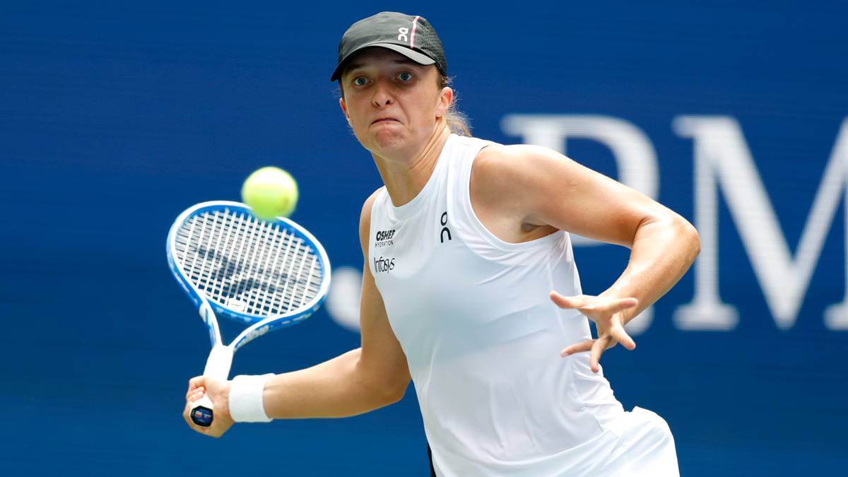 Iga Świątek podczas meczu tenisowego, uderza rakietą piłkę tenisową.