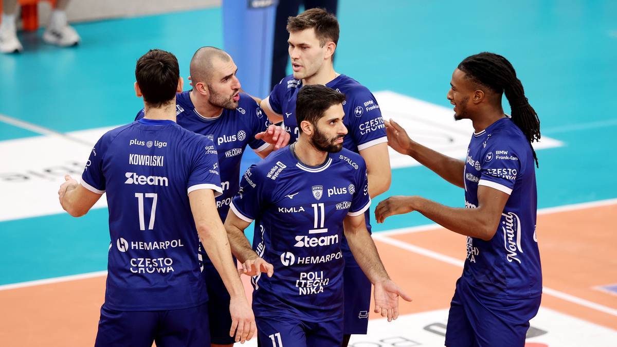 Grupa siatkarzy w granatowych koszulkach dyskutuje na boisku.