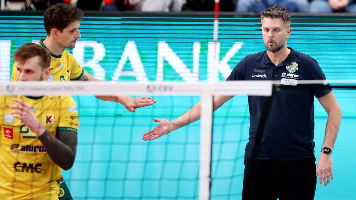 Siatkarze w akcji przy siatce, jeden z nich podaje rękę.