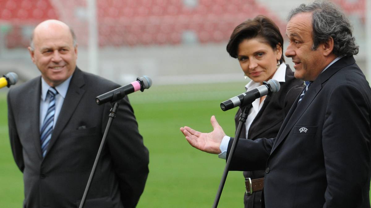 Grzegorz Lato i Michel Platini stoją przy mikrofonach na tle stadionu.