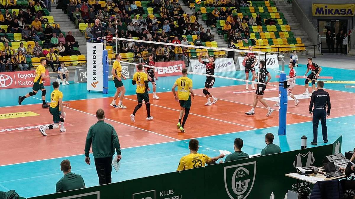 Boisko do siatk&oacute;wki z zawodnikami w trakcie gry, trybuny wypełnione kibicami.