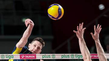 Siatkarz w ż&oacute;łto-niebieskiej koszulce wykonuje atak, podczas gdy drugi zawodnik w białej koszulce pr&oacute;buje go zablokować.