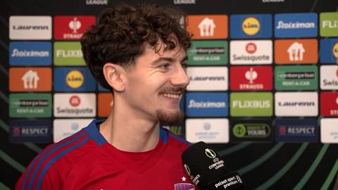 Karol Struski, piłkarz z kr&oacute;tkimi, kręconymi włosami, uśmiecha się do mikrofonu.